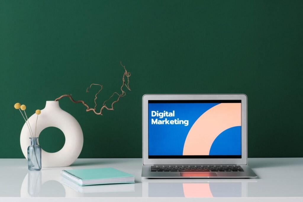 A modern workspace featuring a laptop displaying 'Digital Marketing' against a green wall.